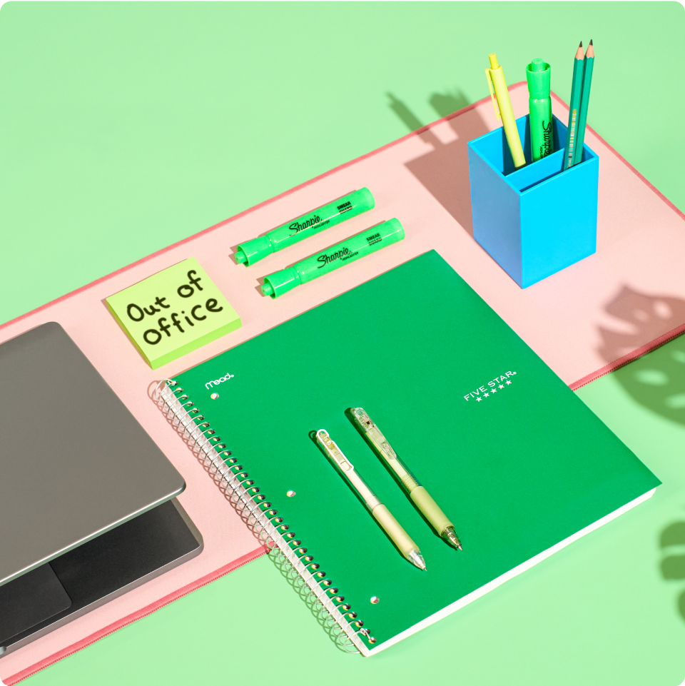 Green notebook, pens, pencils, and laptop on a green background