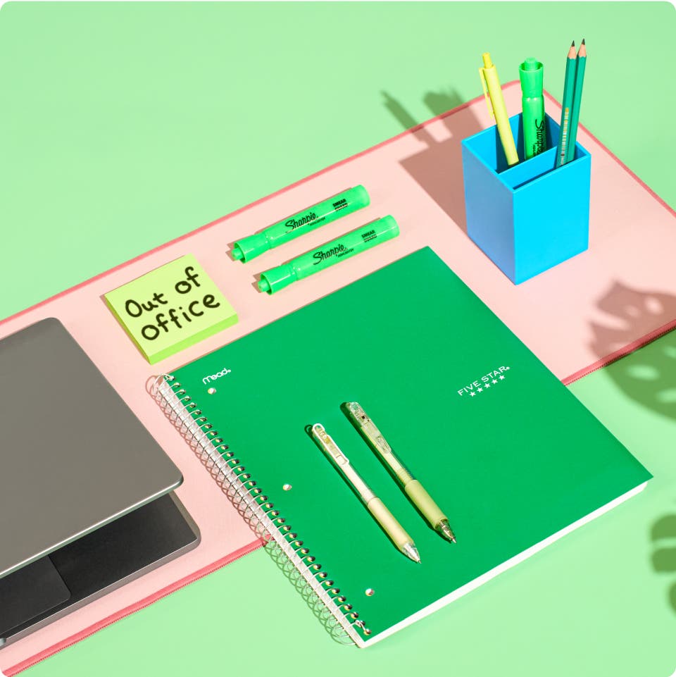 Green notebook, pens, pencils, and laptop on a green background
