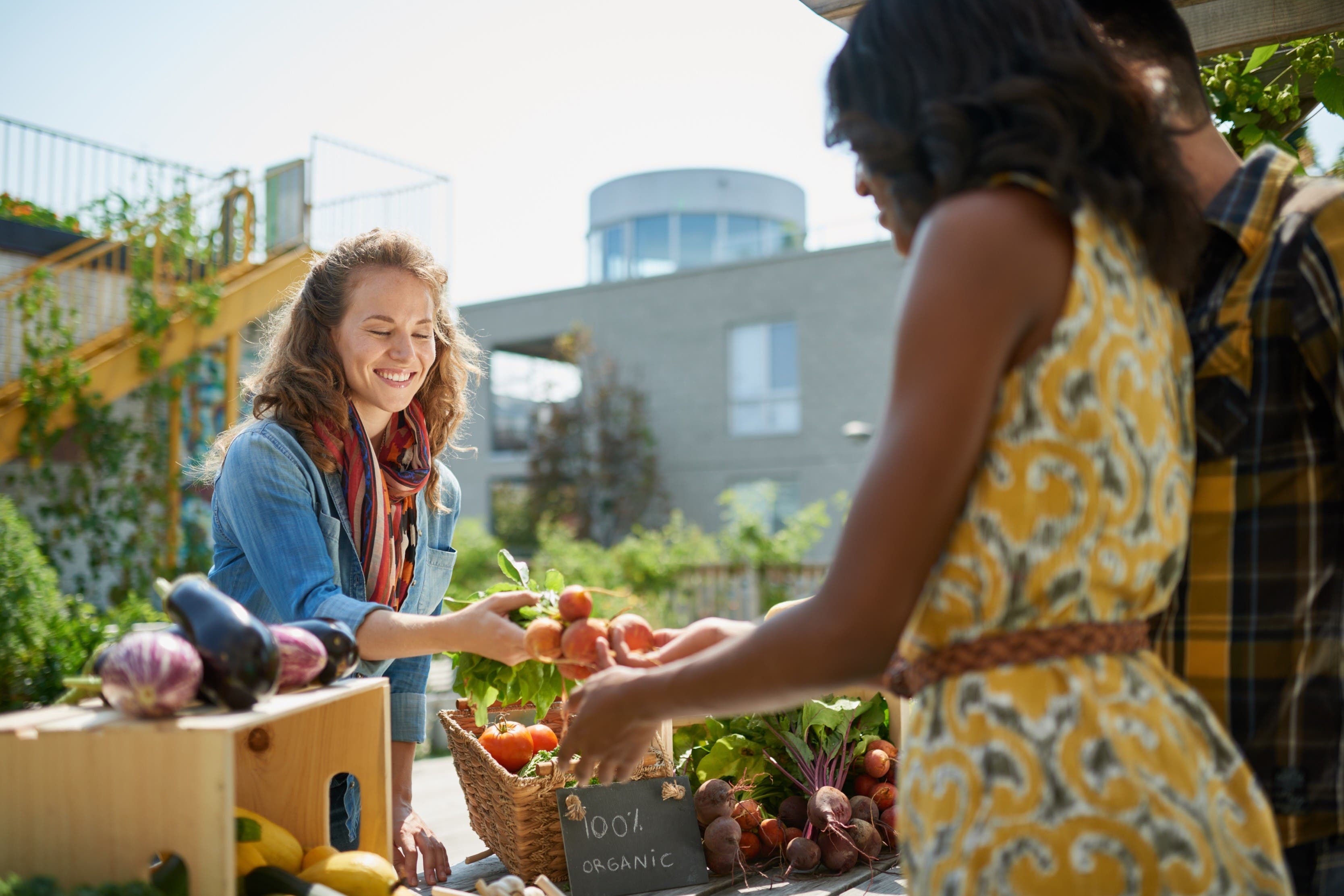 woman handing tomatoes to customer at farmers market