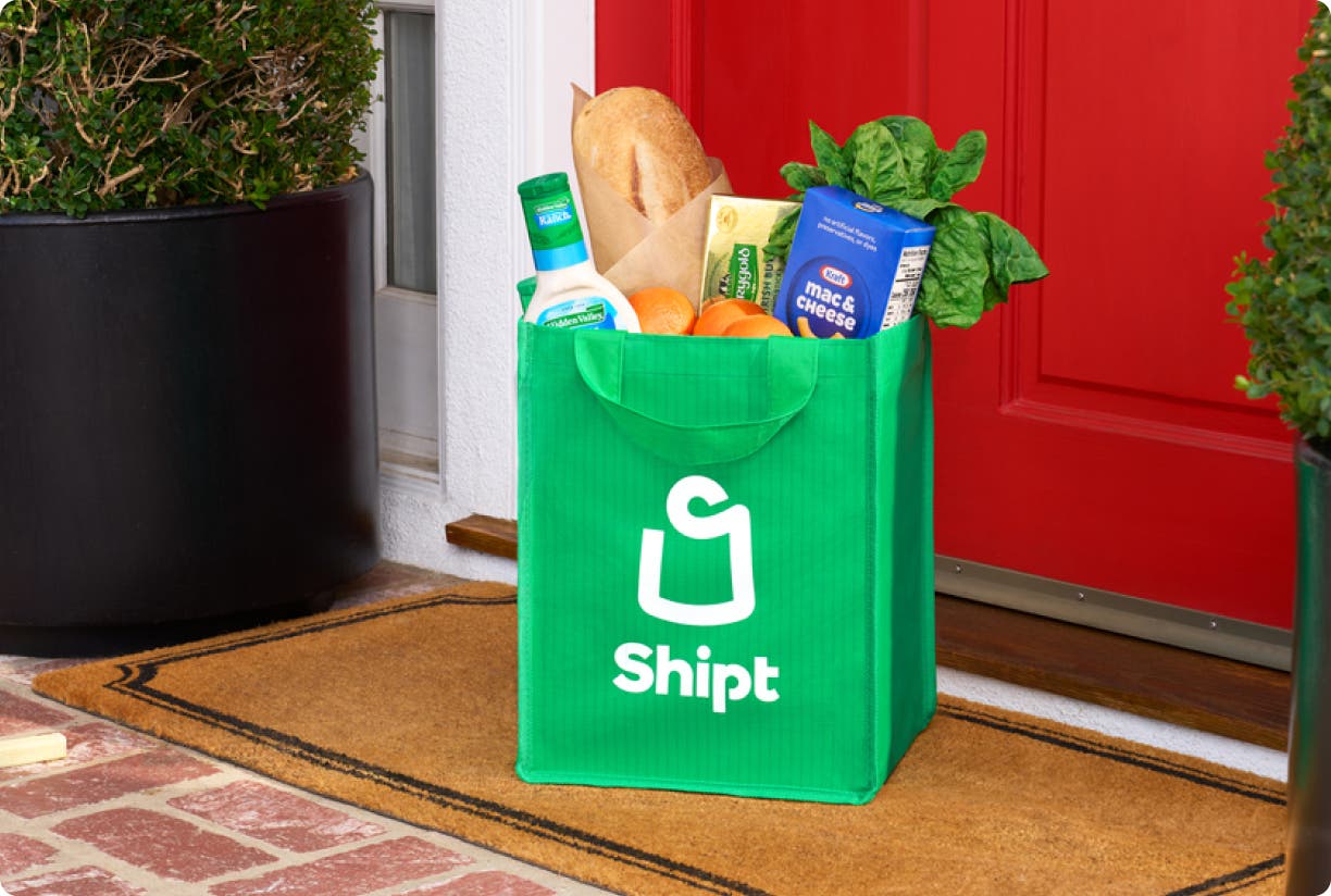 A full bag of groceries in a green Shipt bag at the front door