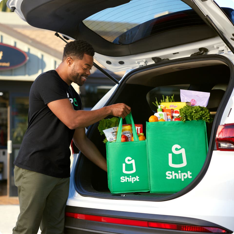 Shipt package delivery person loading trunk of car with Shipt bags