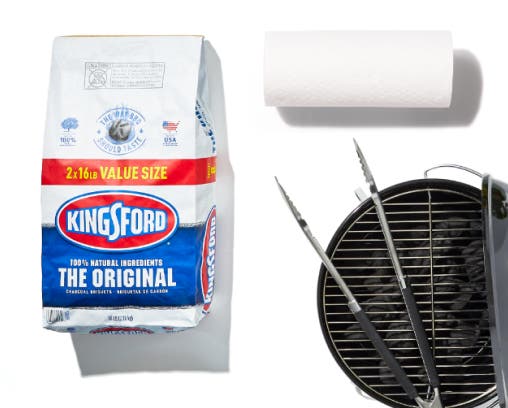 A bag of charcoal, a grill with tongs, and a roll of paper towels