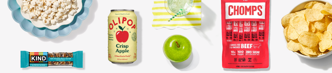 Bowl of pop corn, kind bar, can of olipop soda, green apple, bag of Chomps beef jerky, bowl of chips