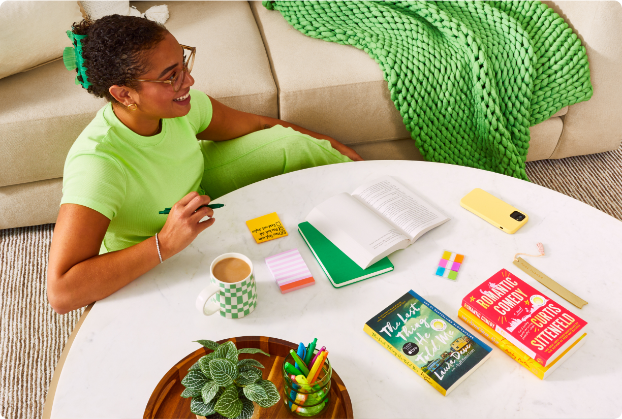 Woman sitting at living coffee table with coffee, notebooks, and pens