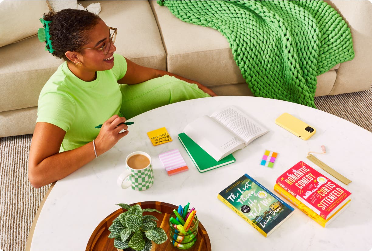 Woman sitting at living coffee table with coffee, notebooks, and pens