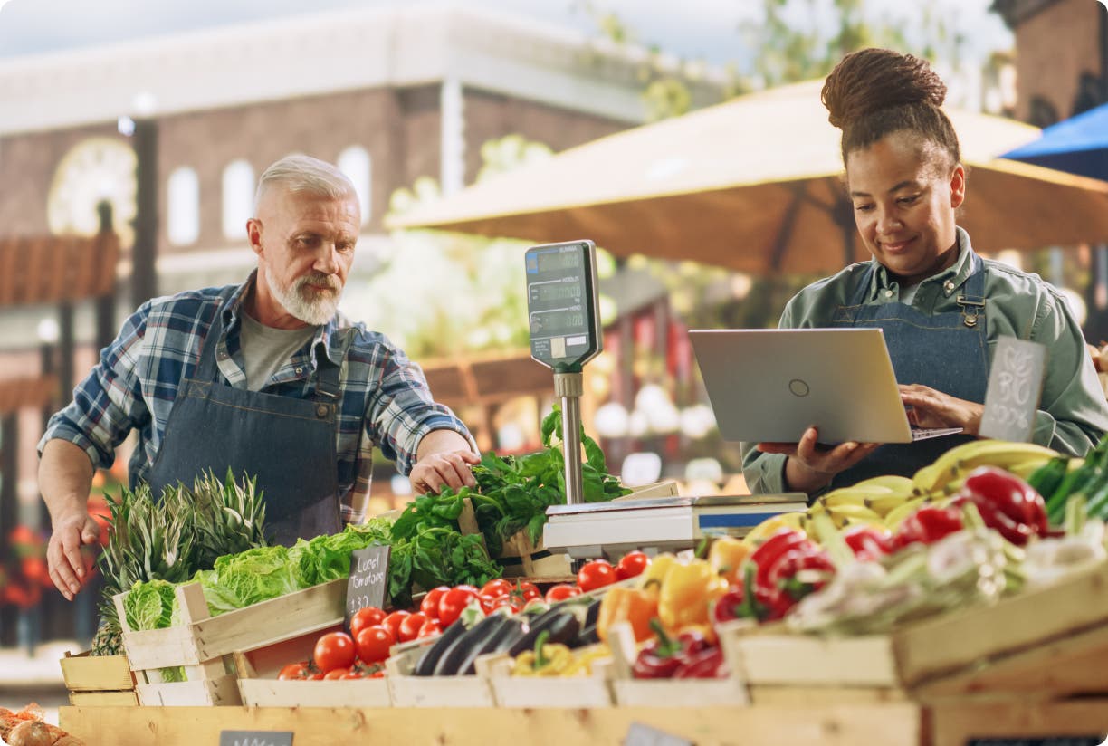 two people standing behind wood bins of fruit and vegetables