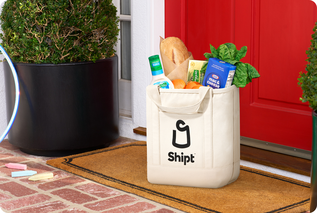 A grocery bag on the mat at a red front door