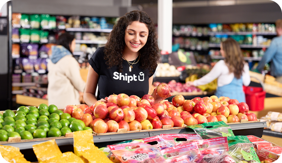 Female shopper with Shipt at the product aisle in a supermarket, picking out apples