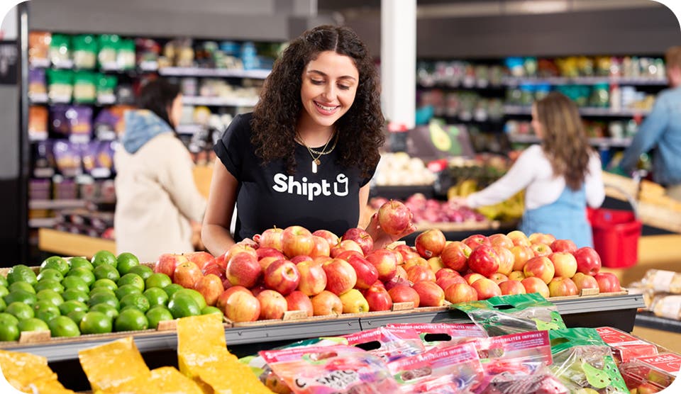 Female shopper with Shipt at the product aisle in a supermarket, picking out apples
