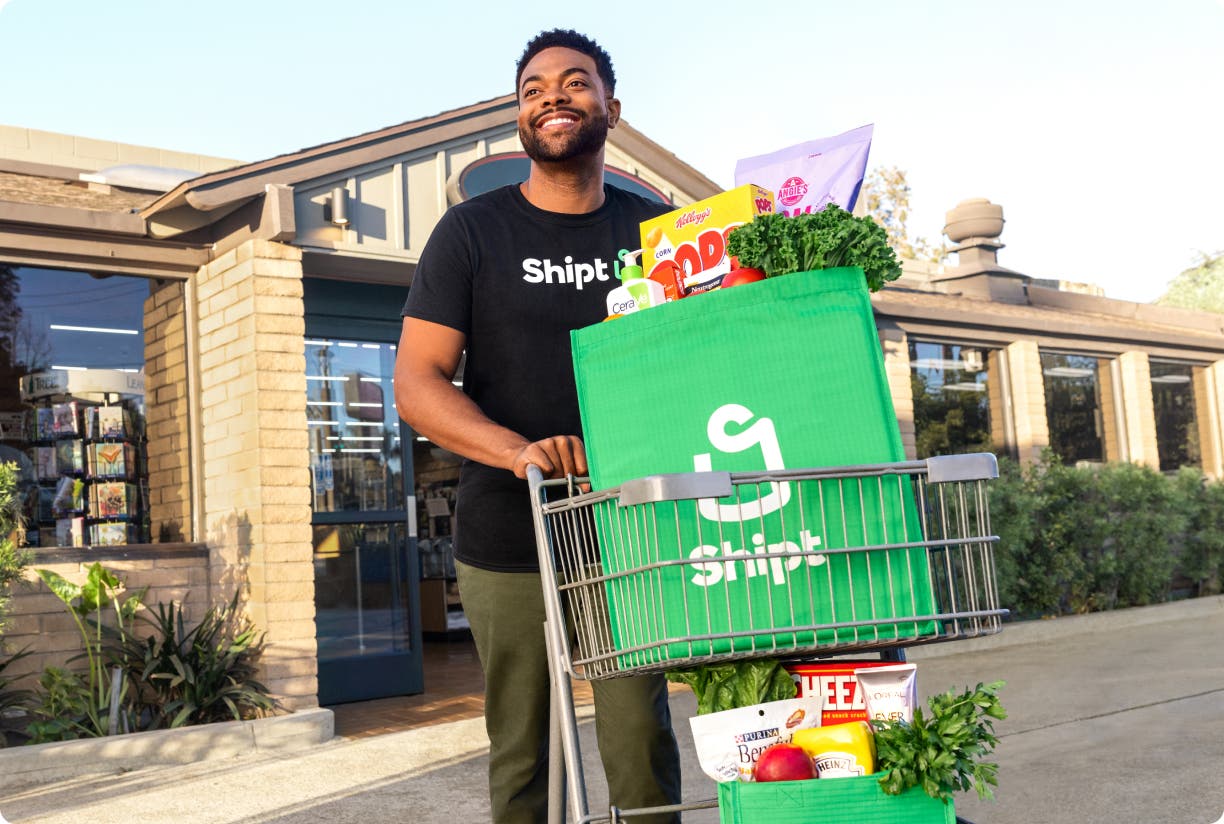 Shopper pushing cart with Shipt grocery bag
