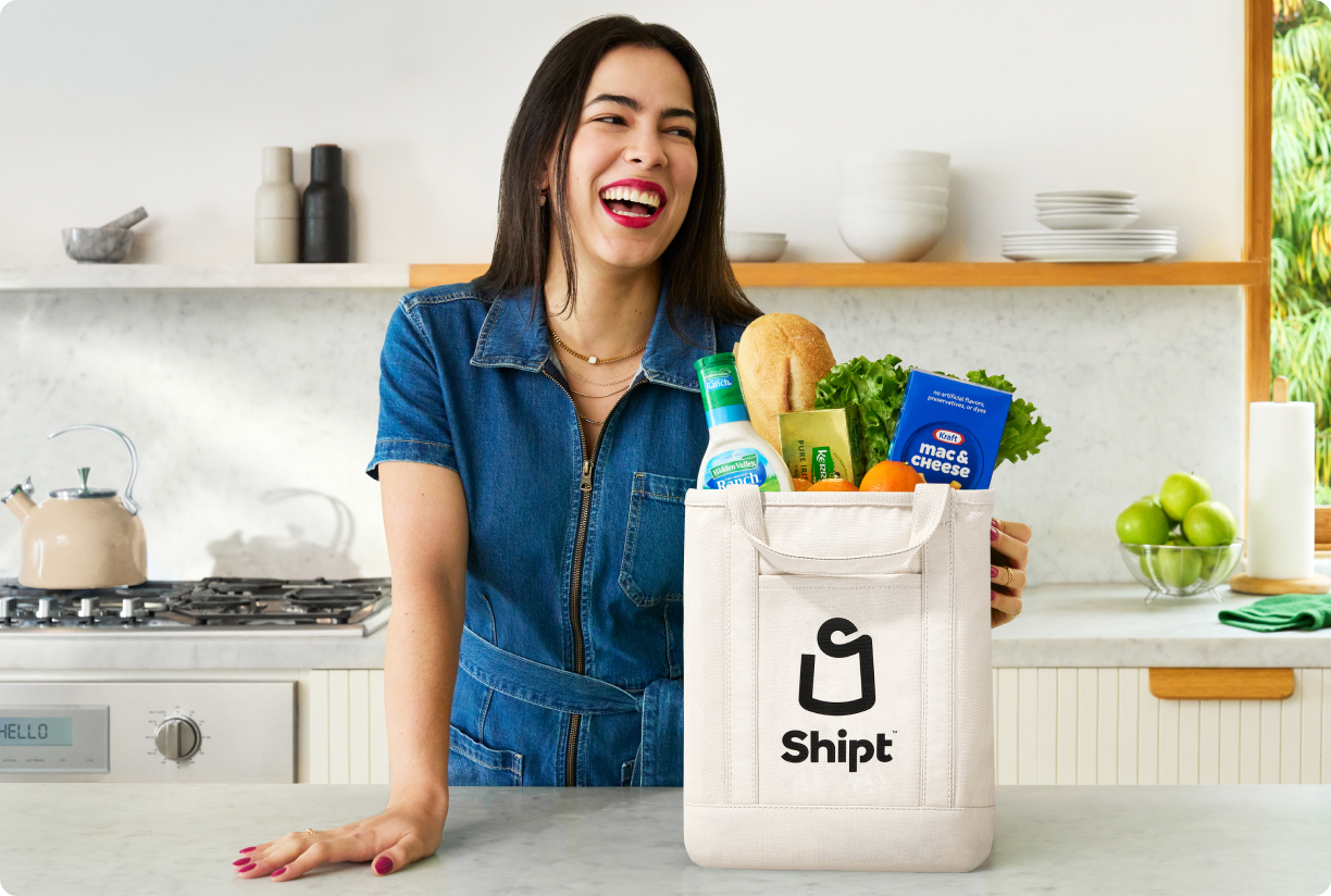 Woman at kitchen counter with Shipt tote bag filled with groceries 