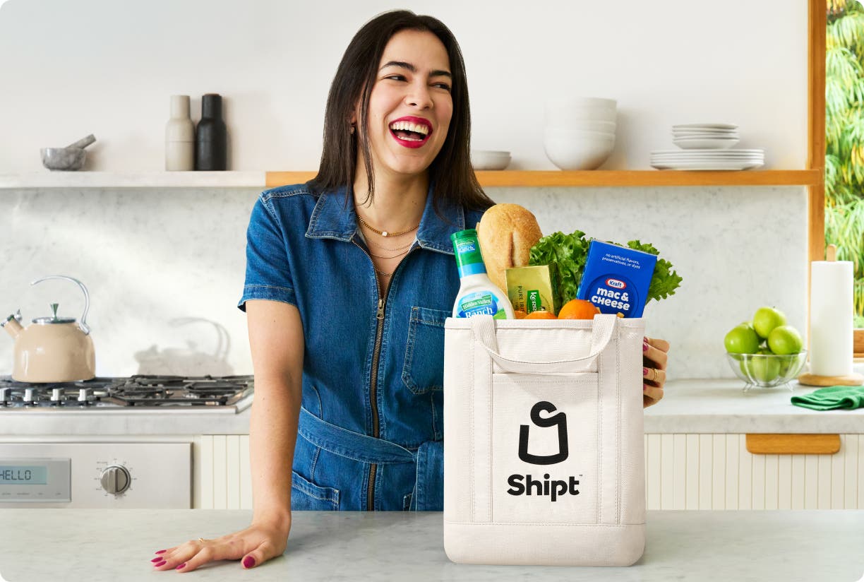 Woman at kitchen counter with Shipt tote bag filled with groceries