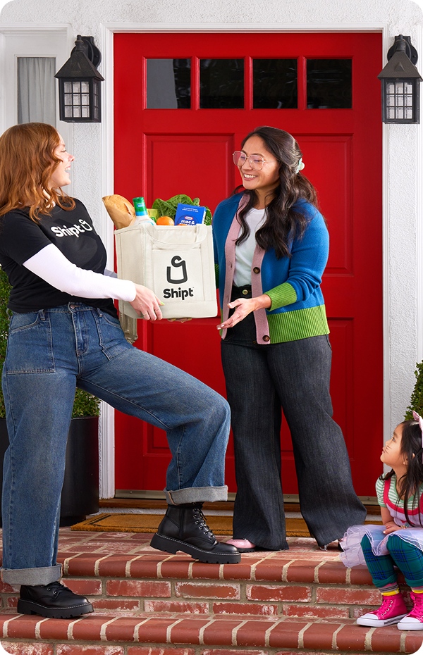 Shopper hands a bag of groceries to a smiling family standing outside their front door.