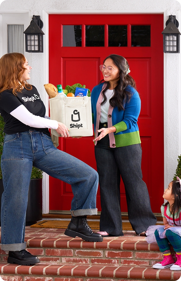 Shopper hands a bag of groceries to a smiling family standing outside their front door.